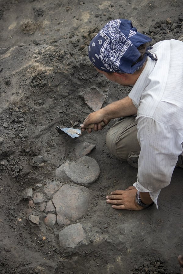 Archaeologists carefully digging and brushing pottery at a site