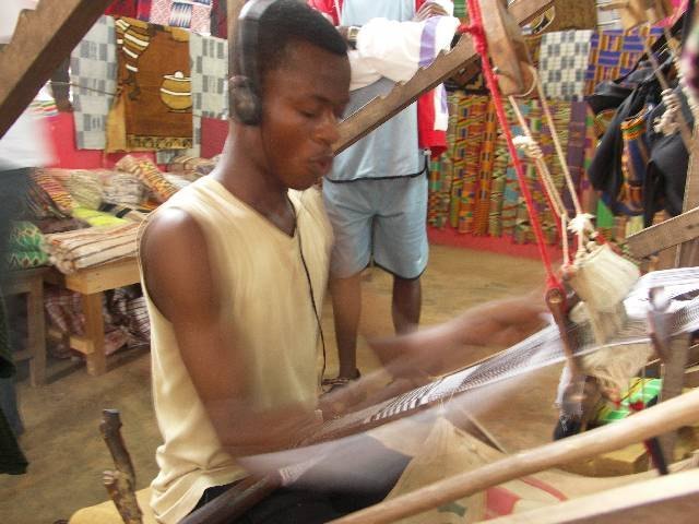 An old weaver at a kente loom under a tree